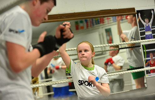 Young teenager in a Sported t-shirt preparing to throw a punch in a boxing ring to the instructor