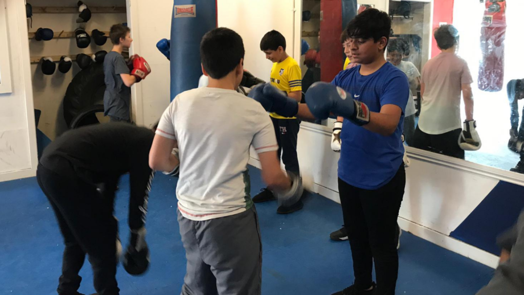 A young people with boxing gloves infront of a punching bag hung from the ceiling