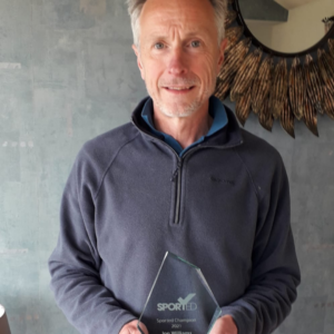 A male in a fleece jumper stands with his glass Sported volunteer award