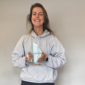 A woman in a grey hoodie stands inside with her glass Sported volunteer award