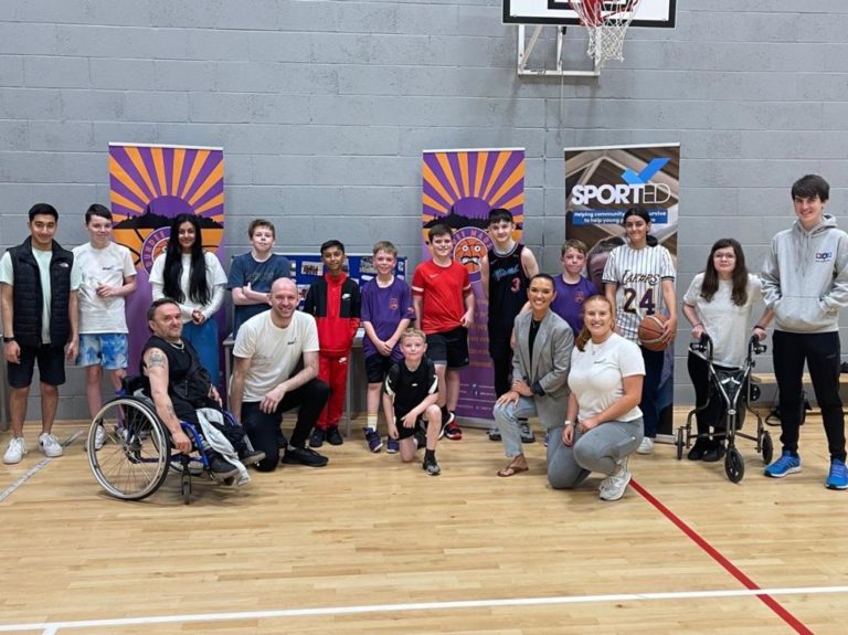 A group of young people and adults smiling to the camera in a sports hall