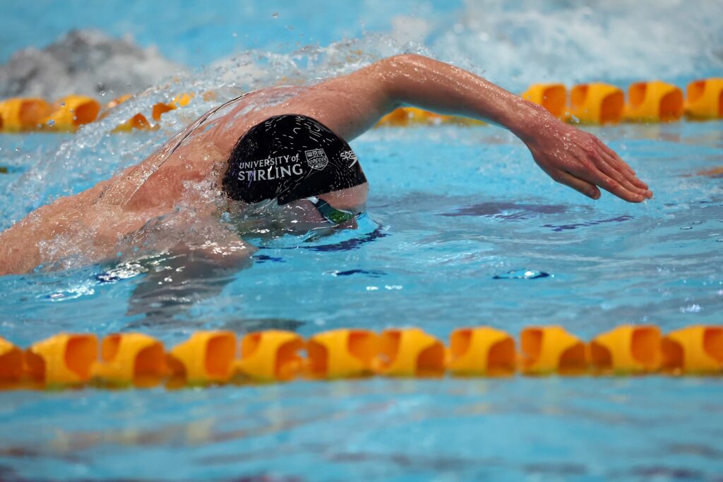 Scottish swimmer Duncan Scott swims in an olympic pool, wearing a black swim cap between two yellow buoy markers
