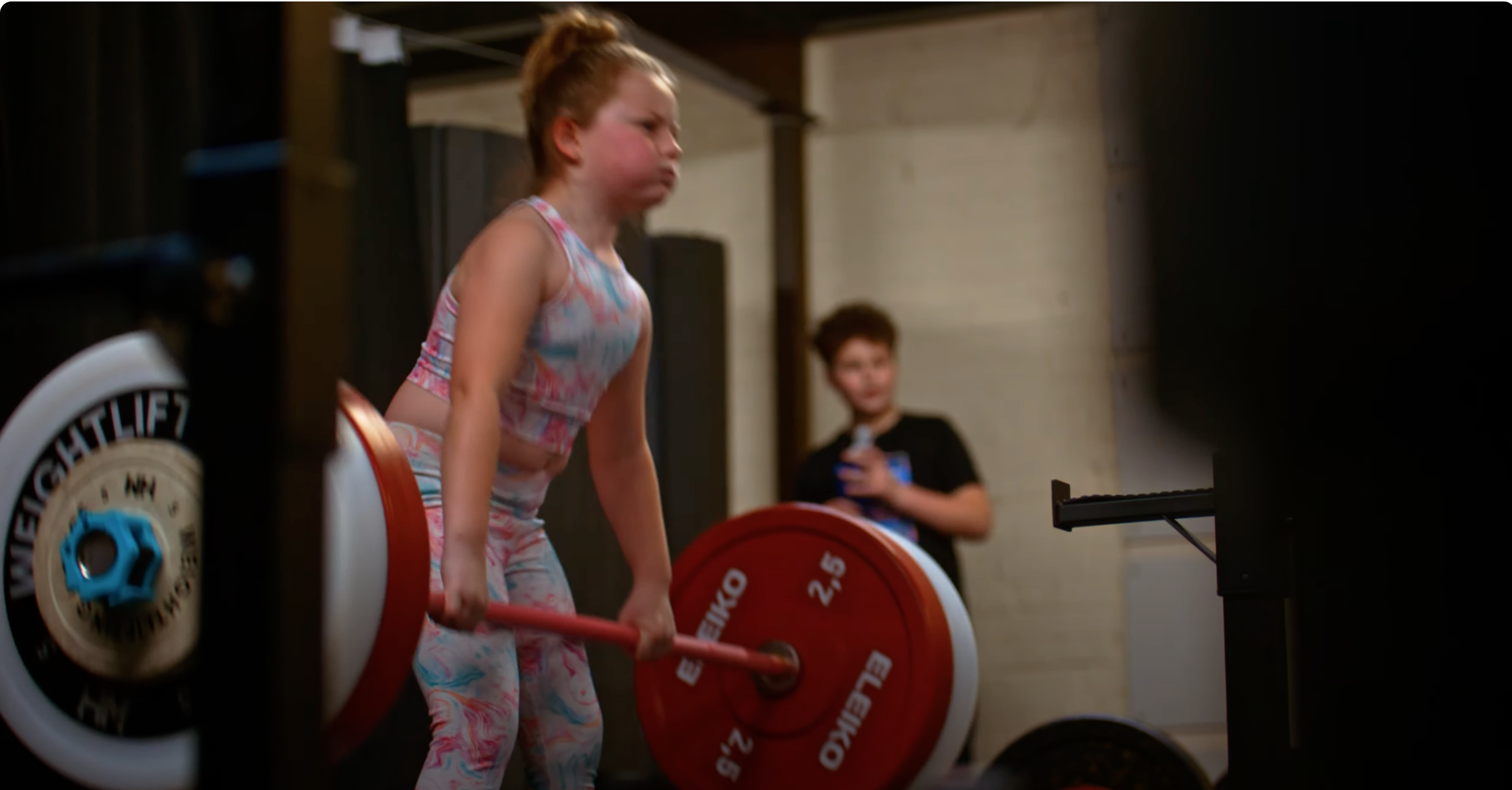 Young girl lifting a barbell with red weights in gym