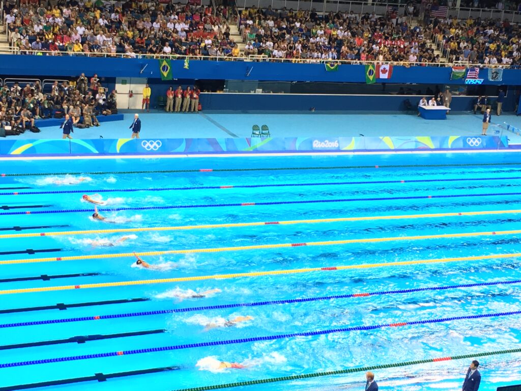 a swimming pool with competitors swimming in lanes. Crowds watching from the stands