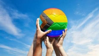 five hands holding up a football coloured with the lgbt+ rainbow flag