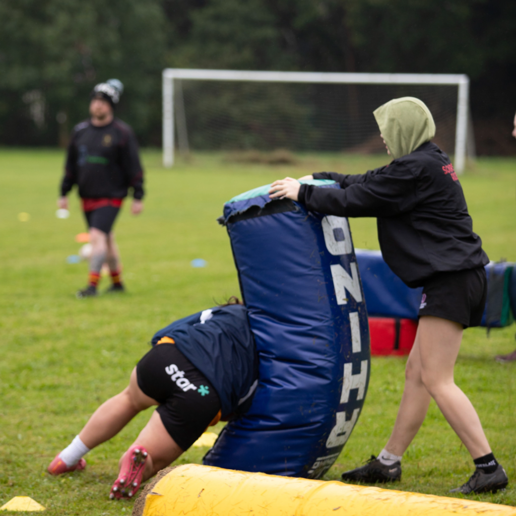 Youth rugby player tackling a rugby tackle bag which is being held up by another youth rugby player