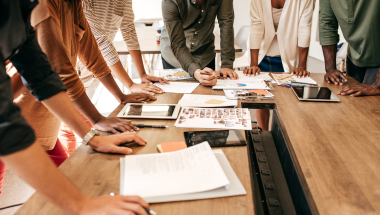 people gathered around a meeting table with tablets and documents