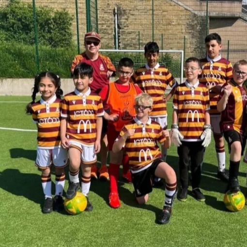 Group of children dressed in Bradford City football club kit which is vertical stripes yellow and burgundy. Smiling and looking proud to be in the team photo.