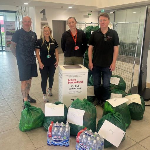 Four adults with bags of donated kit on the floor in front of them