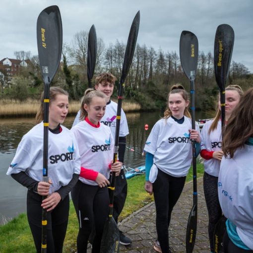 A small group of teenagers holding paddles by open water and trees