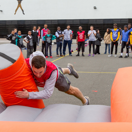 Man rugby tackling an inflatable training bag with group of onlookers in the background