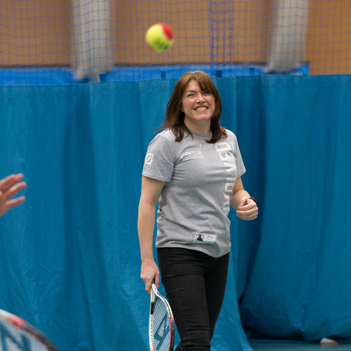 Woman smiling with a tennis racquet having hit a ball