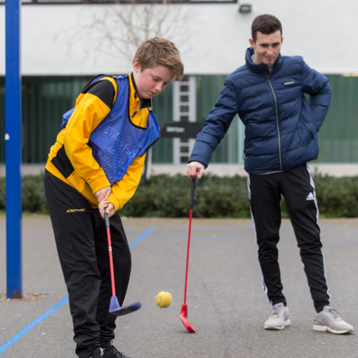Boy hitting golf ball in playground with coach in the background