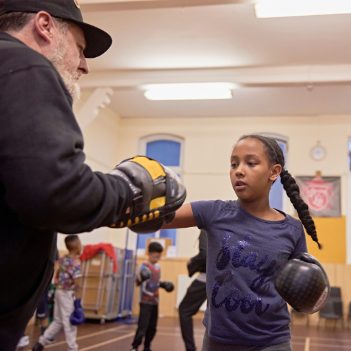 Girl with boxing gloves punching a coach holding a mit