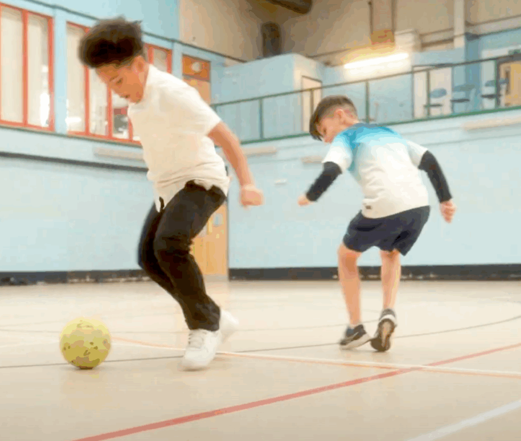 Two young boys playing football in an indoor hall
