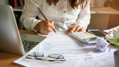 woman working on a document with a calculator and glasses in the foreground