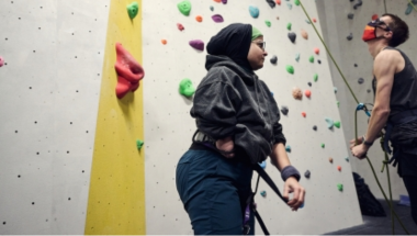 woman with hijab and lower right arm limb difference next to an indoor climbing wall