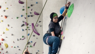 young woman wearing hijab with limb difference climbing on an indoor wall