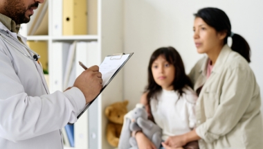 doctor writing on a clip board with a mother and child in the background